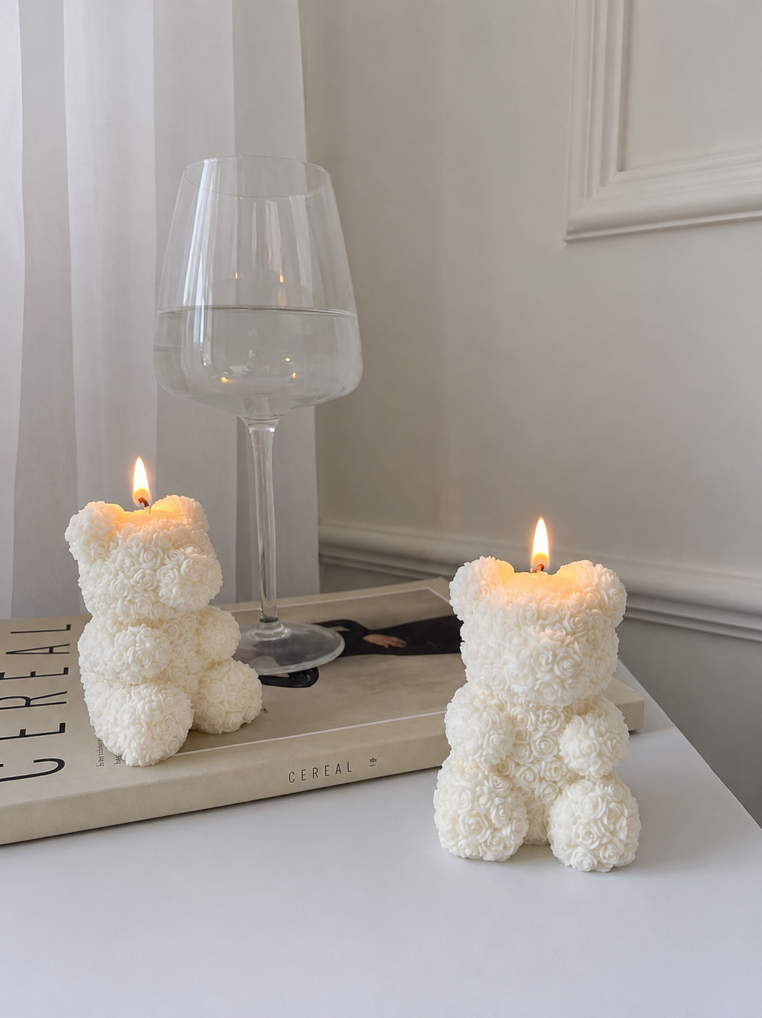 Two bear-shaped candles on a table with a glass of water in the background.